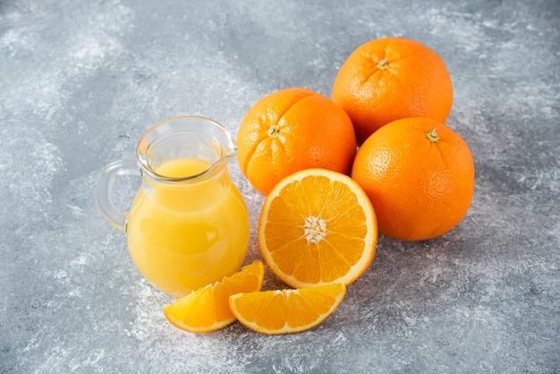 Un pichet en verre de jus avec des fruits orange frais sur table en pierre.