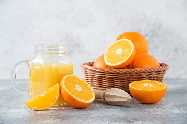 Un pichet en verre de jus avec des fruits orange frais sur table en pierre.