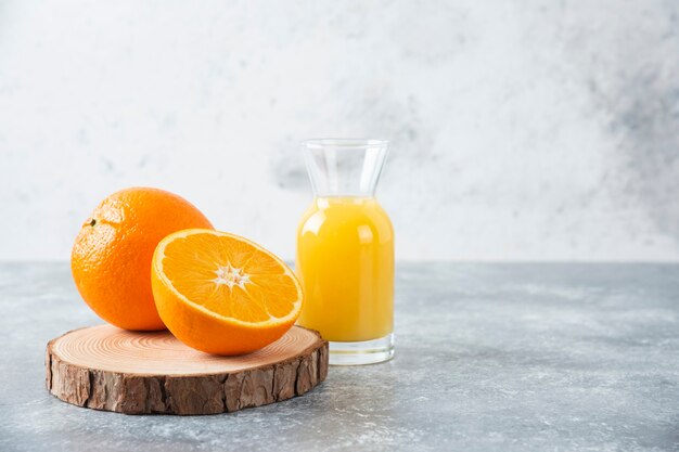Pichet en verre de jus avec des tranches de fruits orange sur une planche de bois.