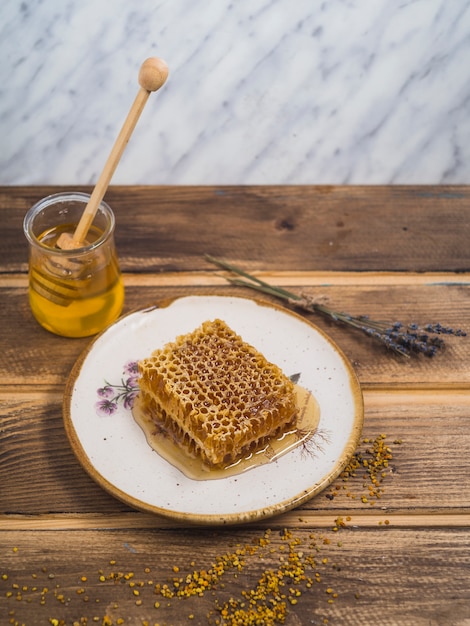 Pièce de miel sur une plaque en bois blanche avec du pollen de lavande et d'abeille sur une table en bois