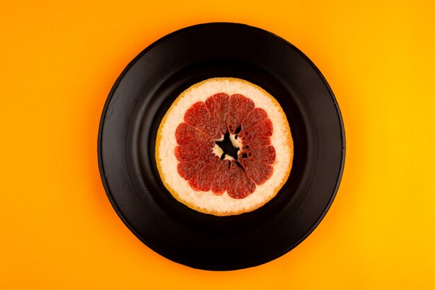 Pièce de pamplemousse rond moelleux juteux frais à l'intérieur de la plaque noire sur l'orange