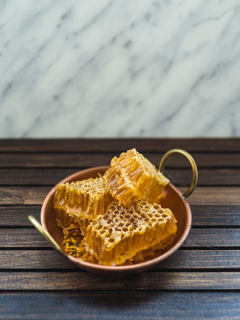 Pièces de peigne de miel frais dans un ustensile en cuivre sur une table en bois