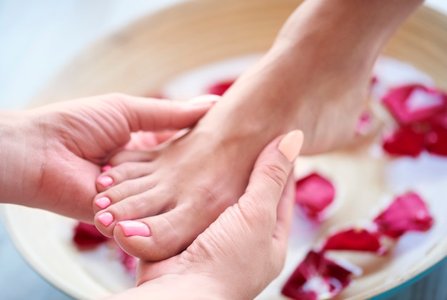 Pieds de femme dans un bol avec de l'eau et des pétales