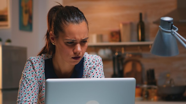 Un pigiste fatigué plisse les yeux en lisant des e-mails travaillant de la cuisine à la maison tard dans la nuit devant un ordinateur portable. Employé concentré occupé utilisant le réseau de technologie moderne sans fil faisant des heures supplémentaires par écrit, searc