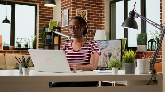 Une pigiste travaillant sur un ordinateur portable pour envoyer des e-mails à distance depuis son domicile, en utilisant une connexion réseau en ligne. Femme d'affaires faisant du travail à distance sur ordinateur, assis au bureau. Emploi indépendant.