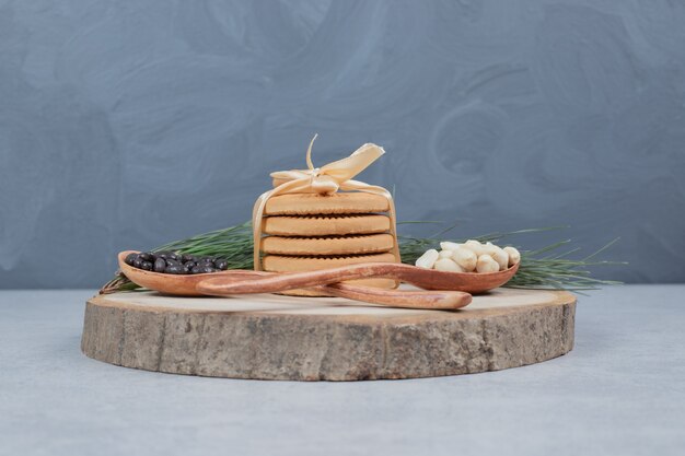 Pile de biscuits attachés avec ruban, cacahuètes et morceaux de chocolat sur planche de bois. Photo de haute qualité