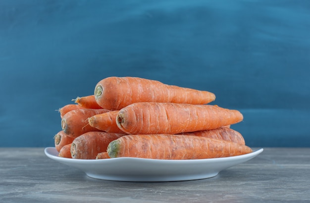 Une pile de carottes dans l'assiette, sur la table en marbre.