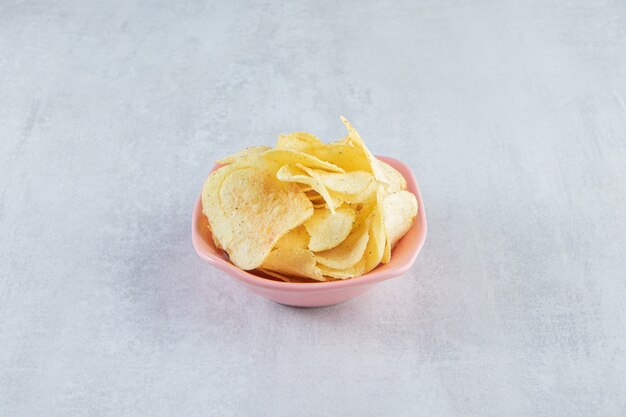 Pile de chips croustillantes salées placées dans un bol rose sur pierre.