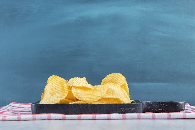 Pile de délicieuses chips d'ondulation sur une planche à découper noire.