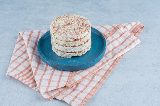 Pile de gâteaux de riz soufflé sur une plaque en bois sur une serviette sur du marbre.