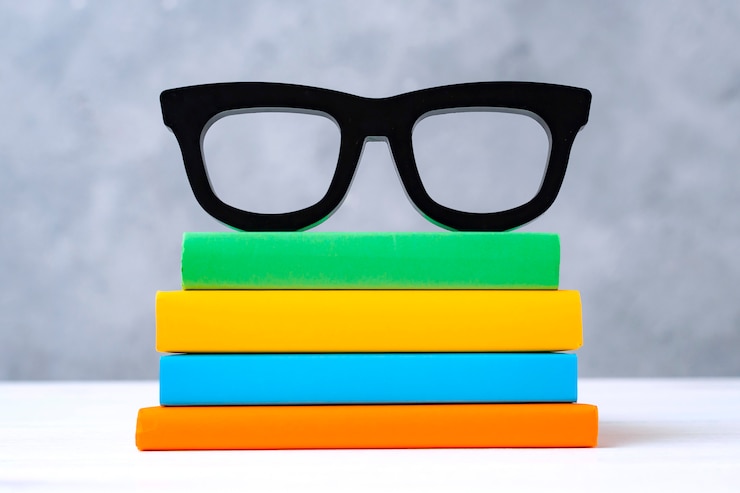 Photo gratuit pile de livres colorés avec des lunettes sur une table en bois blanc contre un mur gris. le concept de retour à l'école, lecture, bibliothèque, littérature, étude, éducation.