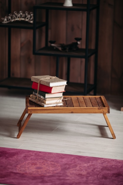 Une pile de livres différents sur une petite table en bois dans la pièce lumineuse près du tapis violet