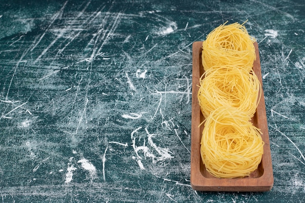 Photo gratuite pile de nids de spaghettis crus sur planche de bois. photo de haute qualité