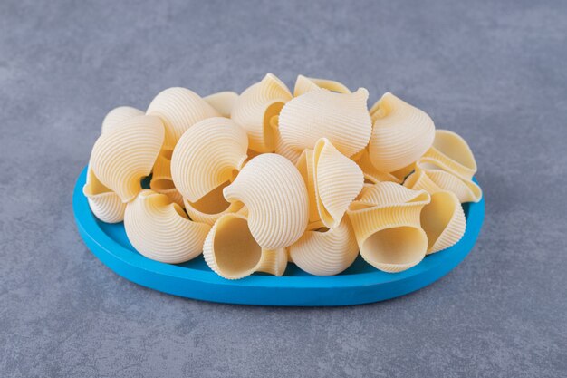 Pile de pâtes conchiglie sur plaque bleue.