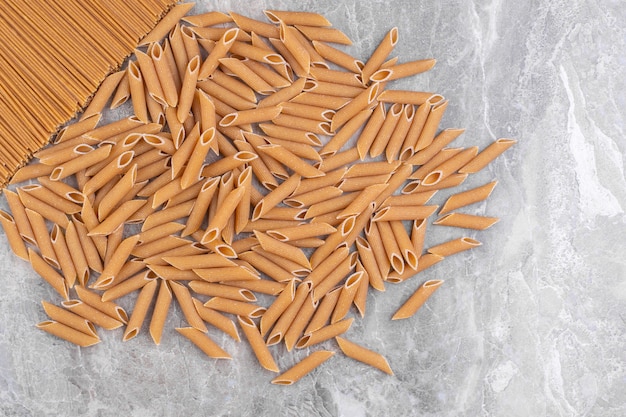 Pile de pâtes penne brunes placées sur une surface en marbre.