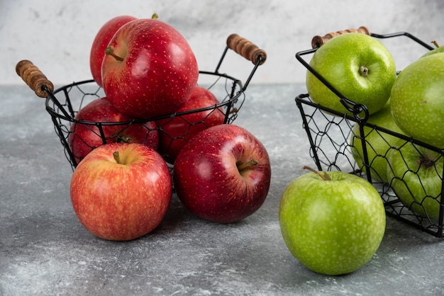 Pile de pommes vertes et rouges fraîches placées dans des paniers métalliques.