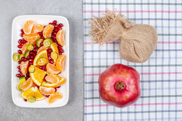 Pile de tranches de fruits frais bio avec grenade entière sur table grise. Vue de dessus.