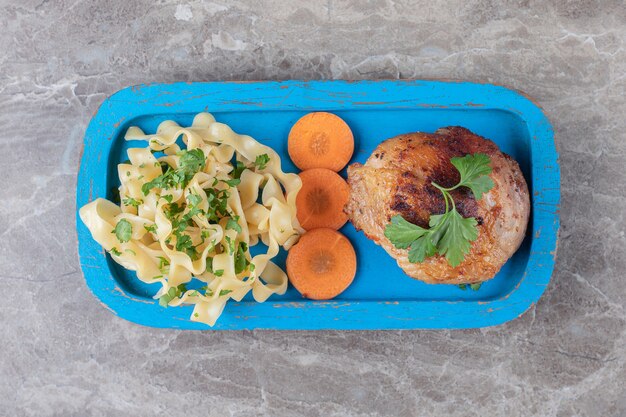 Pilon de poulet cuit, carottes tranchées et pâtes sur plaque de bois, sur le marbre.