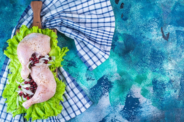 Pilon de poulet mariné aux arilles de grenade sur une feuille de laitue sur une planche sur un torchon sur fond bleu. photo de haute qualité