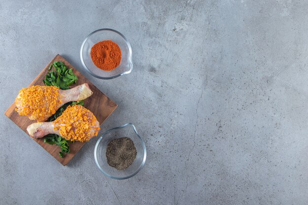 Pilon de poulet mariné sur une verdure sur une planche, sur le fond de marbre.