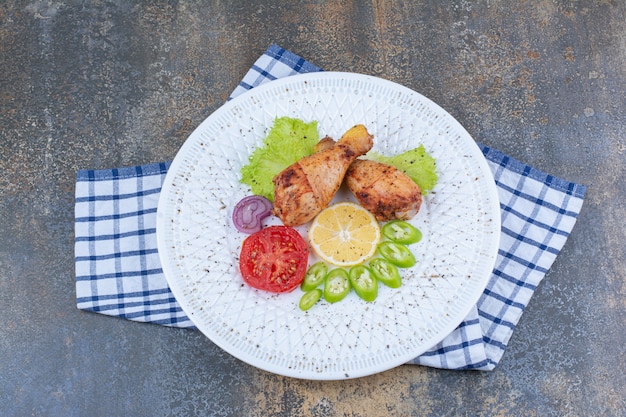 Pilons de poulet grillé sur plaque blanche avec des légumes.