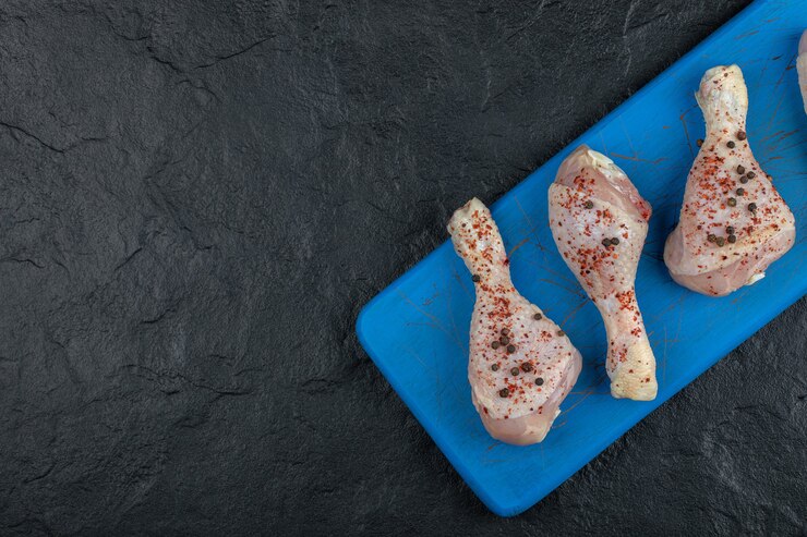 Photo gratuit pilons de poulet marinés sur planche de bois bleue.