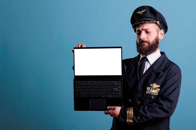 Pilote d'avion sérieux montrant un ordinateur portable avec écran blanc vide, publicité de logiciel d'académie d'aviation, pc avec maquette de site Web d'aéroport. Capitaine d'avion tenant un ordinateur portable avec écran vierge