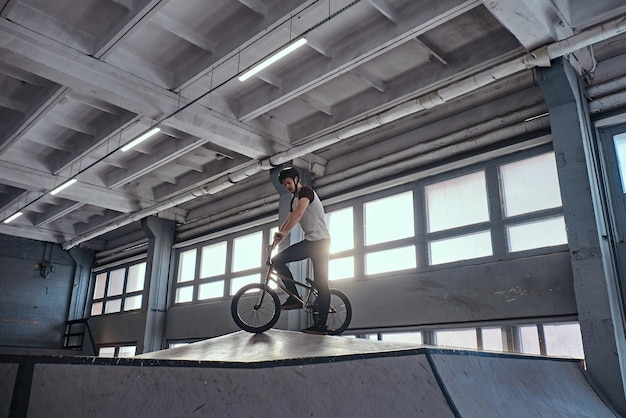 Photo gratuite pilote professionnel de bmx dans un casque de protection se préparant à sauter dans un skatepark à l'intérieur