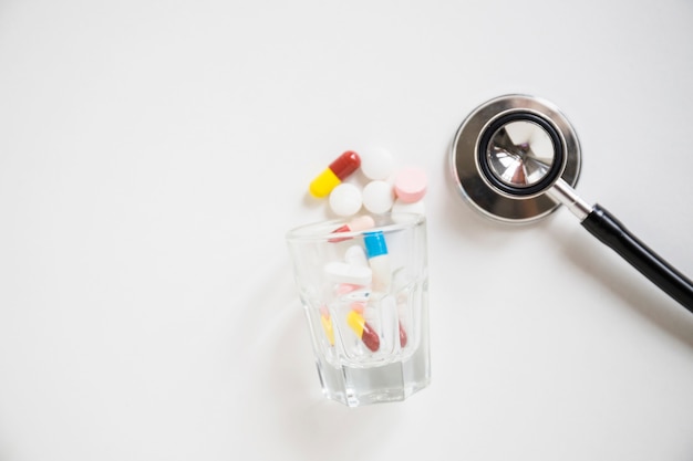 Pilules colorées et capsules renversant avec stéthoscope sur fond blanc