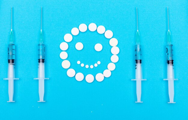 Pilules formant des emoji heureux avec des aiguilles autour