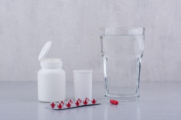 Pilules rouges, récipients et verre d'eau sur une surface en marbre. photo de haute qualité