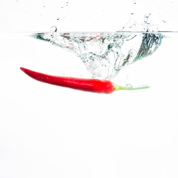 Photo gratuite le piment rouge tombe profondément sous l'eau avec une grande éclaboussure