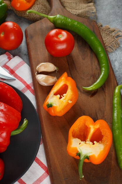 Piments, poivrons jaunes, tomates et ails sur une planche de bois. Vue de dessus.