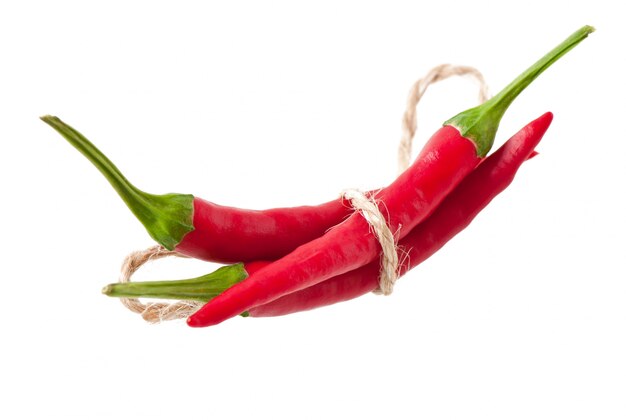 Piments rouges chauds attachés avec une corde sur blanc