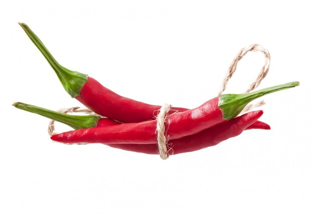 Piments rouges chauds attachés avec une corde sur blanc