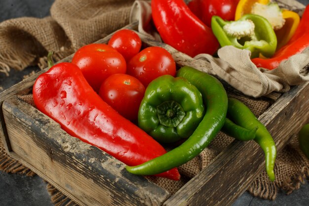 Photo gratuite piments verts et rouges aux tomates dans un plateau en bois.