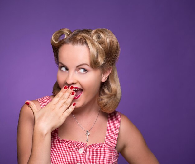 Pin-up suspecte souriante et fermant la bouche isolée sur violet. Modèle blonde sexy en détournant les yeux et en pensant aux secrets.