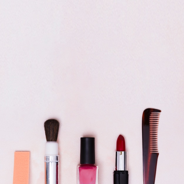 Pinceau de maquillage; bouteille de vernis à ongles; rouge à lèvres et peigne sur fond texturé blanc