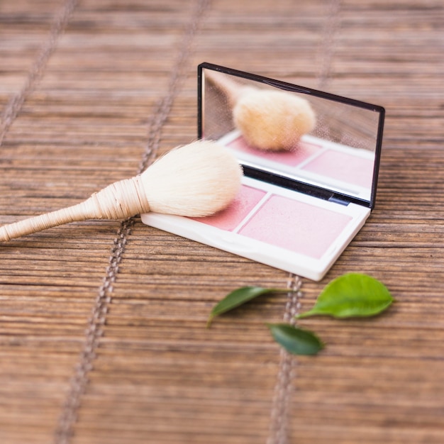 Pinceau de maquillage avec un fard à joues rose et des feuilles sur un napperon