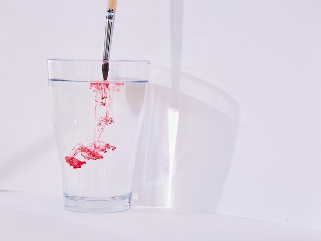 Un pinceau avec de la peinture rouge colore une eau dans le miroir en couleur rouge