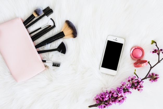 Pinceaux de maquillage avec smartphone; Poudre faciale compacte et rameau de fleurs sur fourrure blanche