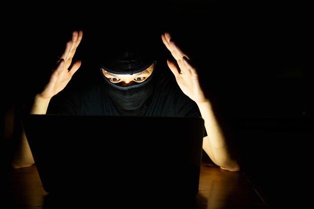 Pirate informatique faisant son travail avec un ordinateur portable dans la pièce sombre