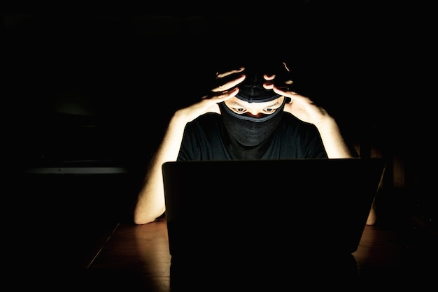 Pirate informatique faisant son travail avec un ordinateur portable dans la pièce sombre