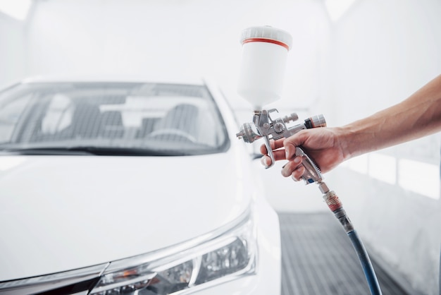 pistolet avec de la peinture dans les mains d'un homme pour peindre une voiture