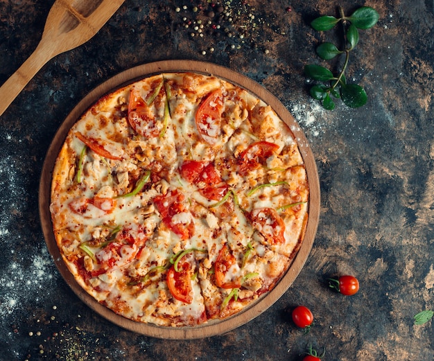 pizza au poulet avec poivrons, tomate, fromage sur planche de bois ronde