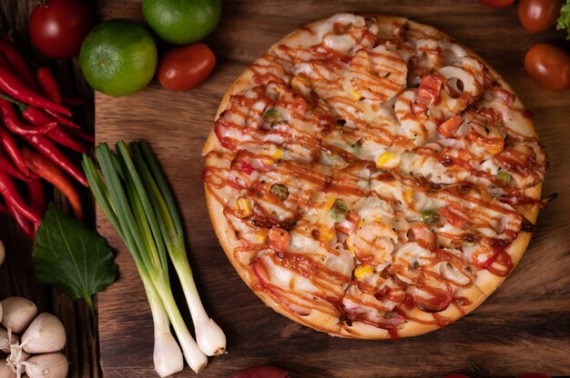 Pizza aux saucisses, maïs, haricots, crevettes et bacon sur une assiette en bois