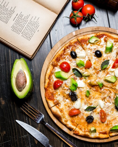 Pizza à l'avocat sur planche de bois fromage tomate basilic épices olives vue de dessus