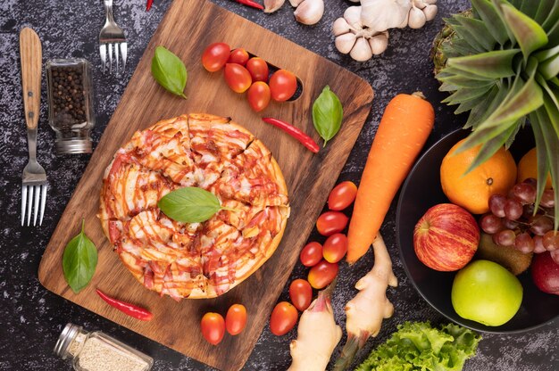 Pizza dans un plateau en bois avec tomates Chili et basilic.