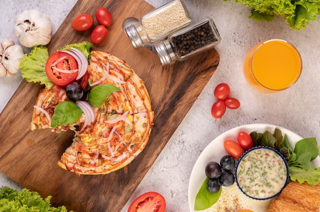 Photo gratuite la pizza est dans un plateau en bois garni d'oignons rouges, de raisins noirs, de tomates et de laitue.