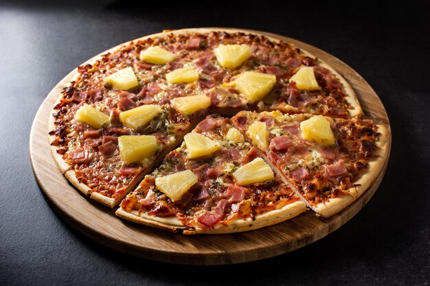 Pizza hawaïenne avec jambon d'ananas et fromage sur fond d'ardoise noire